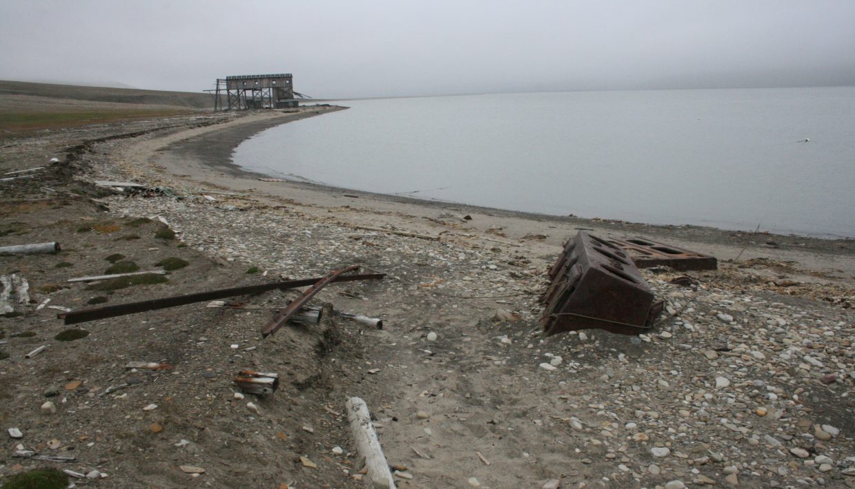 Foto som viser skinnegangen til trallebanen. Kysterosjon har undergravd skinnegangen slik at skinner og lokomotiv i dag ligger nede på stranden.