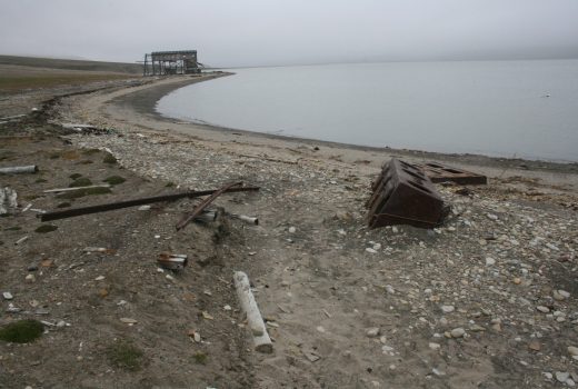 Foto som viser skinnegangen til trallebanen. Kysterosjon har undergravd skinnegangen slik at skinner og lokomotiv i dag ligger nede på stranden.