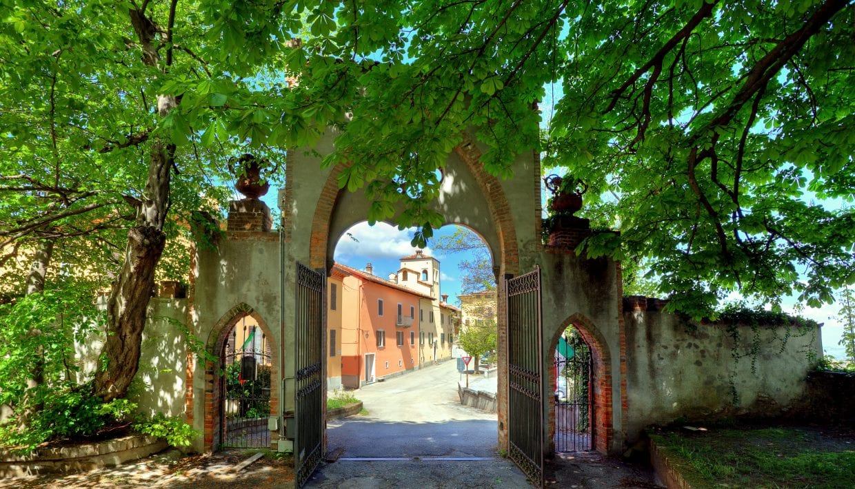 Old gate under the trees at the entrance to Novello town center in Piedmont, Northern Italy.