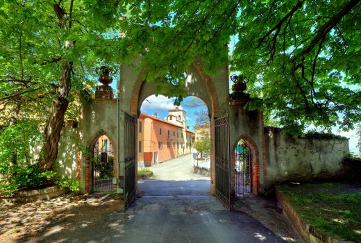 Old gate under the trees at the entrance to Novello town center in Piedmont, Northern Italy.
