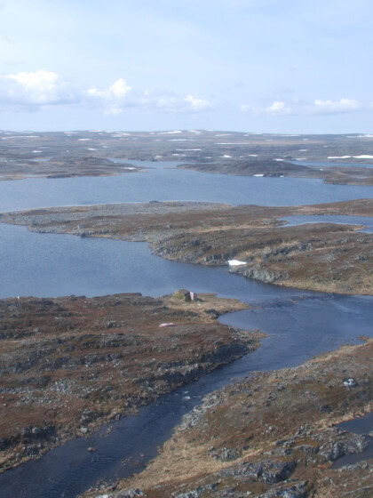 Bildet viser et landskap fra Finnmark, med fjord og holmer sett i fugleperspektiv. Vannet og himmelen er blått, mens landdelene bører preg av tidlig høst.
