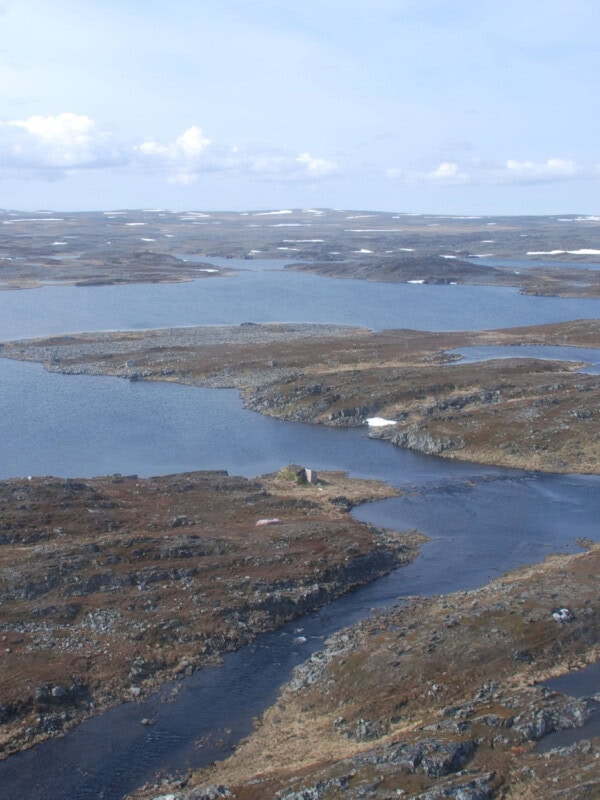 Bildet viser et landskap fra Finnmark, med fjord og holmer sett i fugleperspektiv. Vannet og himmelen er blått, mens landdelene bører preg av tidlig høst.