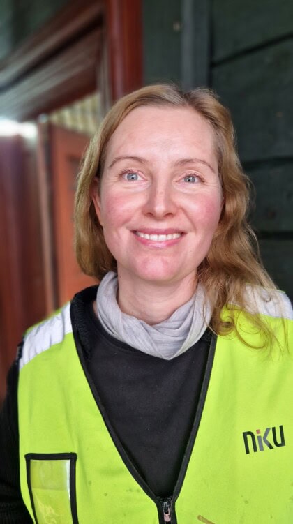 Portrett av konservator Anne Apalnes Ørnhøi fra NIKU. Hun har blondt hår og er iført en gul refleksvest. Bildet er tatt inne i Finnegården , Bryggen i Bergen.