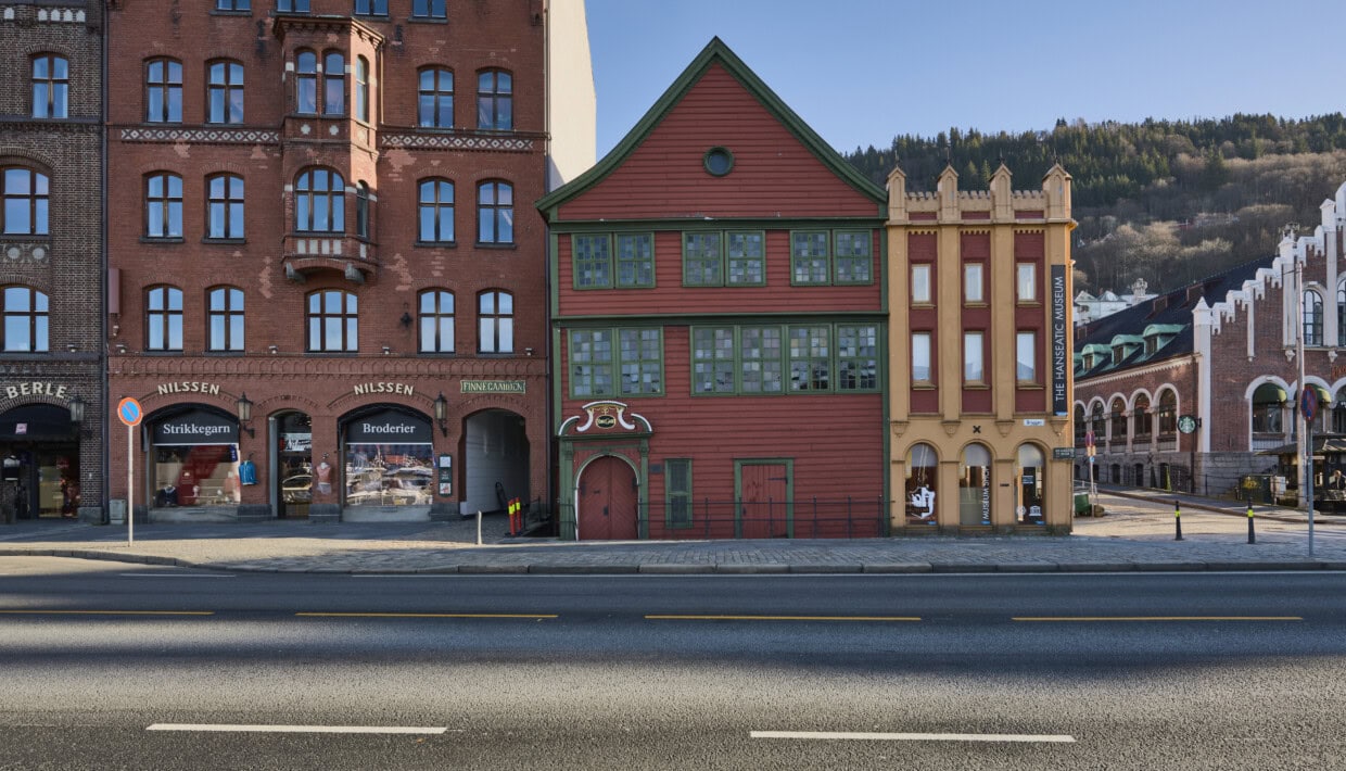 Bildet viser fasaden på noen av bygningene på Bryggen i Bergen, nærmere bestemt den røde og grønne Sjøstuen og den røde og gule Murtasken, begge del av Finnegården som huser det Hanseatiske museum. Været er pent.