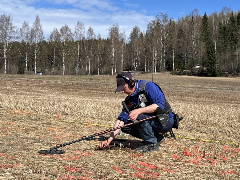 Metalldetektorist Rune Sætre plukker opp mynter på Mørstadjordet, 2026. Han sitter på huk, og rundt han er det markert sirkler på bakken. I disse sirklene har metallsøkeren gjort utslag på mynter. 