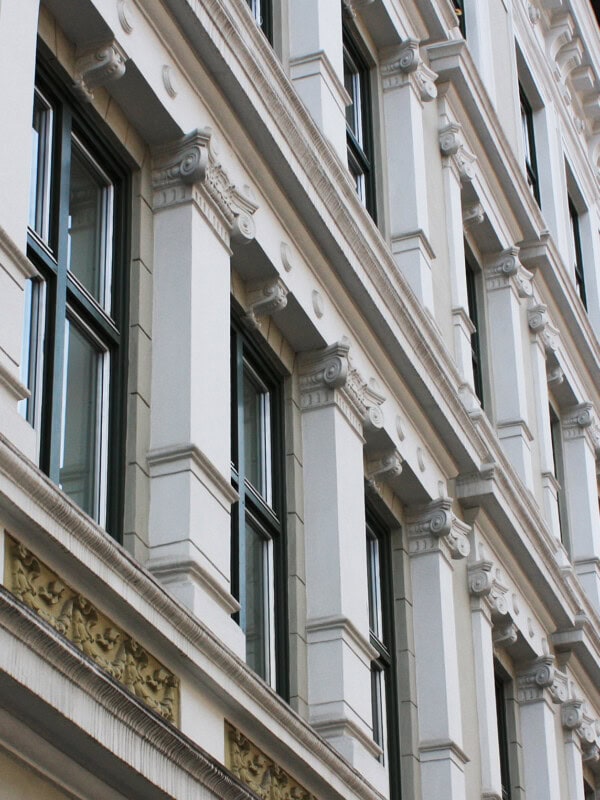 Vindusfasade med arkitektoniske detaljer. Murgården er fra 1800-tallet, og fargen er lys gråbaige. 